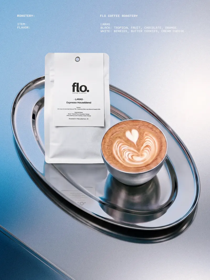 A flat white with latte art beside a flo. espresso blend pouch on a chrome tray.